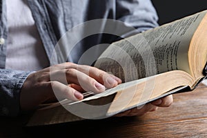 Man reading holy Bible at wooden table, closeup