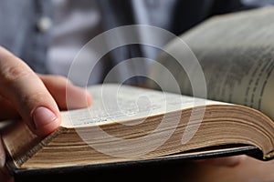 Man reading holy Bible at wooden table, closeup