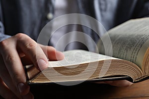 Man reading holy Bible at wooden table, closeup