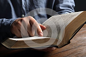 Man reading holy Bible at wooden table, closeup