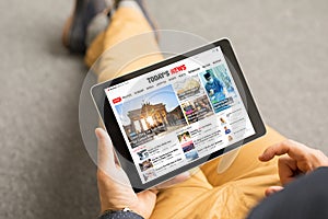 Man reading news website on tablet. All contents are made up.