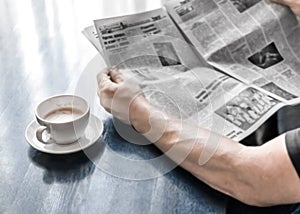 A man reading newspaper and drinking coffee sitting in cafe or at home in kitchen at morning time. A coffee cup on dark