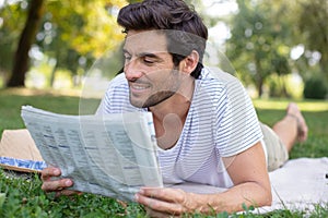 man reading newspaper while sitting on green meadow