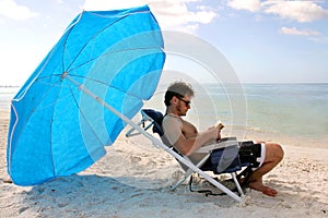 Man Reading by Ocean Under Beach Umbrella