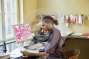 Man Reading Papers By Computer In Office