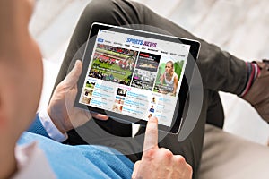 Man reading sports news on tablet. All contents are made up. photo