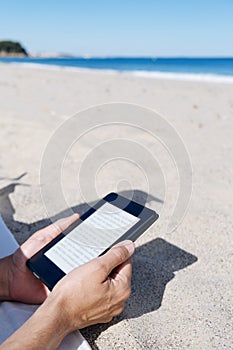 Man reading in a tablet or e-reader on the beach