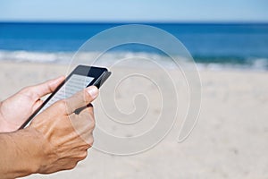 Man reading in a tablet or e-reader on the beach