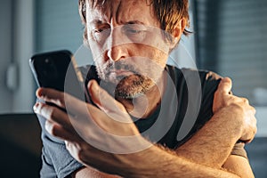 Man reading text message on mobile phone, unkempt male holding cell phone indoors