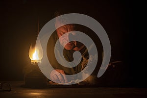 Man reads a book by the light of a kerosene lamp and a domestic cat lies nearby