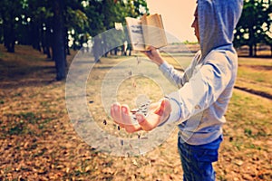 A man reads a book in the park, letters fly from above and fall on his hand, exhaustive knowledge in nature