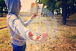 A man reads a book in the park, letters fly from above and fall on his hand, exhaustive knowledge in nature