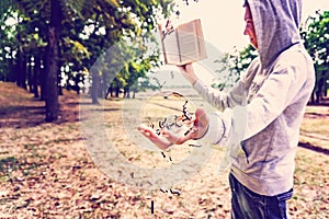 A man reads a book in the park, letters fly from above and fall on his hand, exhaustive knowledge in nature