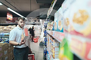 A man reads the product on a package when shopping in a supermarket. A man dies out food at the store