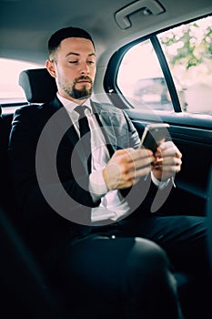 Business Man in rear of the car. Typing text message on cell phone