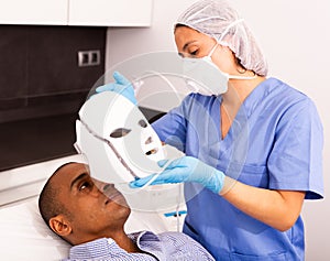 Man receiving facial light therapy in aesthetic medicine office