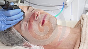 Man receiving facial ultrasound cavitation treatment by cosmetologist