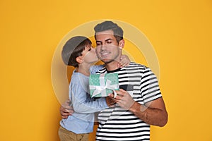 Man receiving gift for Father`s Day from his son on yellow background