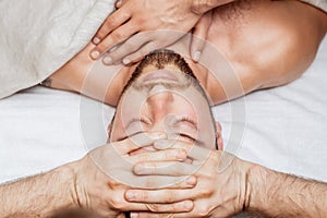 Man receiving head massage by two masseurs