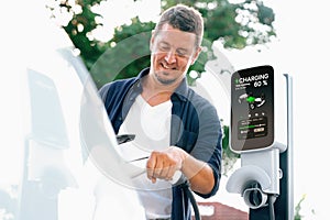 Man recharging battery for electric car during road trip. Exalt