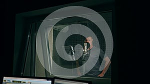 Man In Recording Studio Talking Into Microphone. View through the glass.