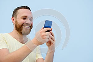 Man with a red beard looks into the phone with surprise and ecstasy a bright summer photo on a blue background