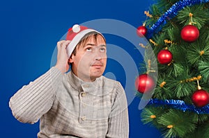 The man in a red cap scratches a nape sitting near a green fir-tree.