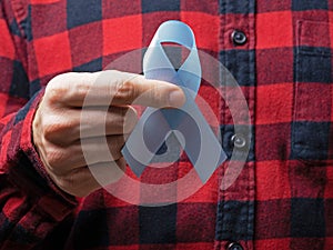 A man in a red checked shirt holds a blue ribbon with both hands-a symbol of prostate cancer awareness.