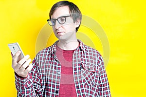 Man in red checkered shirt and glasses looking at smartphone on yellow background