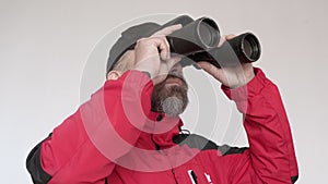 Man in red coad looks ahead through binoculars. Watching faraway objects.