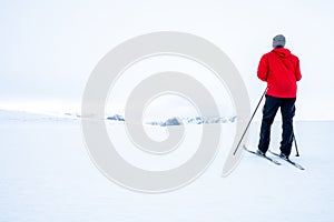 Man in red jacket doing cross country skiing during foggy weather in the mountains of Norway