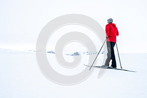 Man in red jacket doing cross country skiing during foggy weather in the mountains of Norway