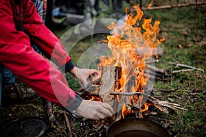 Man in the red jacket placing a firewood to the campfire