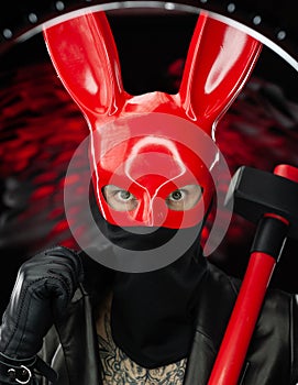 A man in a red rabbit mask in a leather cloak with an axe