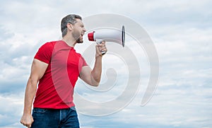 man in red shirt shouting in loudspeaker on sky background