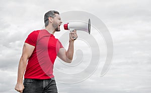 man in red shirt shouting in loudspeaker on sky background