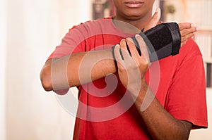 Man in red shirt wearing black wrist brace support on right hand and gripping arm with other