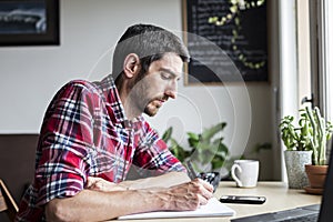 Man in red shirt writing at a desk