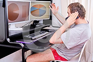 A man in red shorts is sitting at home at the computer and talking on the phone. The concept of remote work during the quarantine