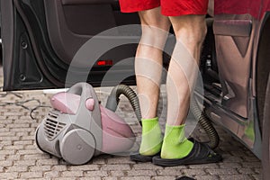 Man in red shorts using vacuum cleaner inside a car. Domestic male hores. Cleaning of car interior, seats, door.