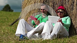 Man with red smartphone and woman with Tablet-PC sits near a haystack