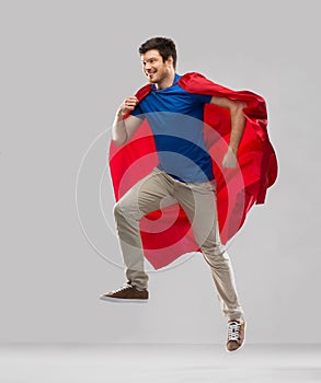 Man in red superhero cape jumping in air