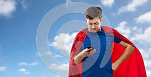 Man in red superhero cape with smartphone over sky