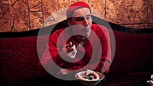 Man in Red Sweater and Beanie Enjoying a Meal at a Cozy Diner. A focused man in a vibrant outfit dines alone, savoring