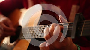 A man in a red sweater plays an acoustic guitar indoors  a close-up view of an wide open aperture