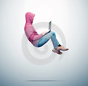 A man in a red sweatshirt, jeans levitates in the air working on a laptop, on blue background. Side view. Computer superiority con