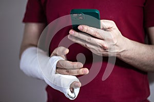 A man in a red T-shirt with a broken arm in a cast holds and uses a phone Close-up
