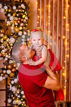 Man in a red T-shirt kisses a baby girl in a red dress for Christmas