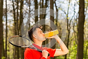 The man in a red t-shirt pose with a tennis racket and drinking water from a thermocouple. Sport concept