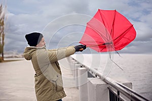 Man with red umbrella caught in gust of wind near river